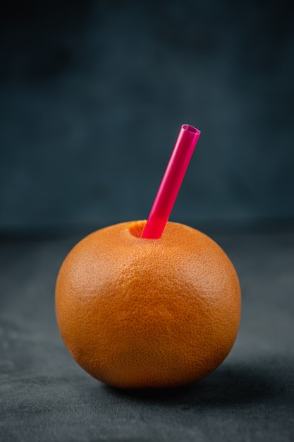 Side view of orange with pink straw on a black blackboard