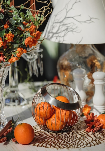 Free photo side view of oranges in metal basket vase on the table