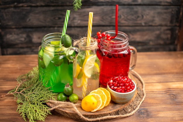 Side view of organic fresh juices in bottles served with tubes and fruits on a wooden cutting board