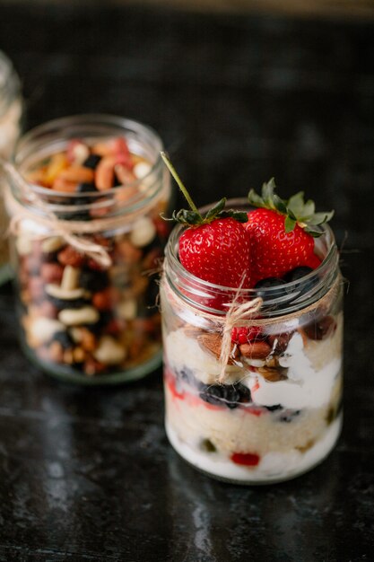 Side view of overnight oats with fresh strawberries blueberries and nuts in a glass jar on dark surface