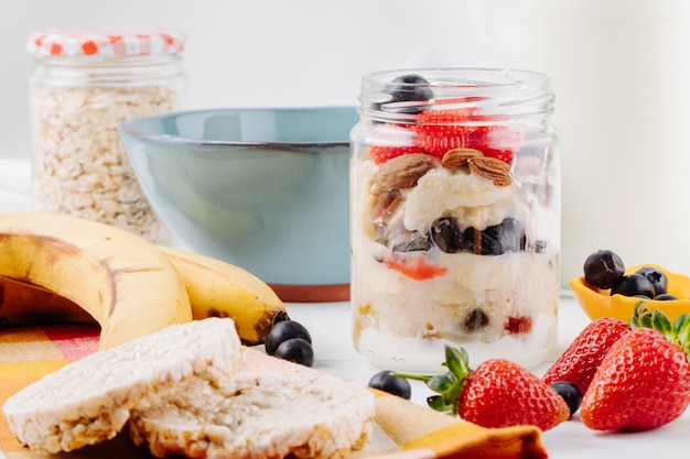 Side view of overnight oats with fresh strawberries blueberries and nuts in a glass jar on rustic table