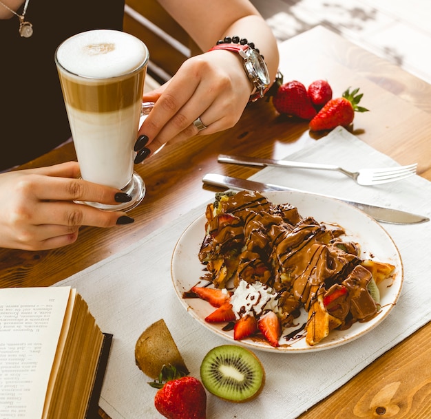 Side view pancakes waffle pancakes with strawberry kiwi chocolate and latte macchiato on the table