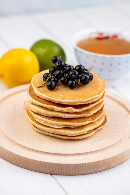 Side view pancakes with black currants on a wooden tray