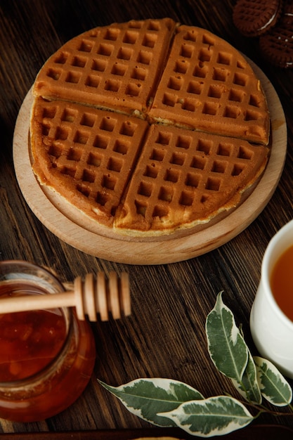 Side view of pancakes with glass jar of jam and cup of orange juice on wooden background