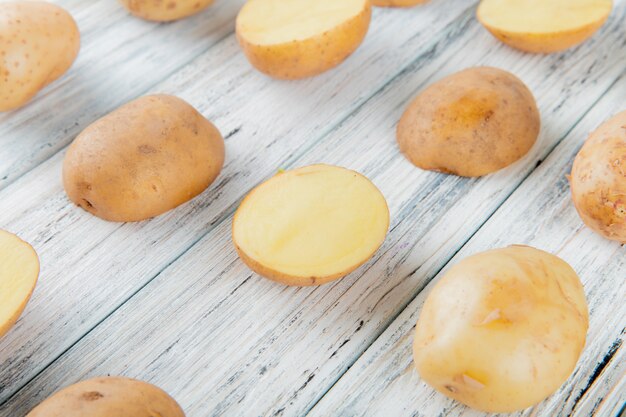 Side view of pattern of whole and cut potatoes on wooden background with copy space