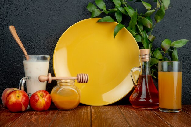 Side view of peaches with glass of yoghurt plum jam peach syrup and juice with empty plate on wooden surface