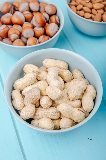 Side view of peanut in shell in a bowl and hazelnuts in a bowl on blue background