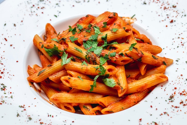 Side view penne pasta with tomato sauce and greens on a plate