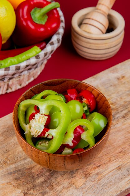 Side view of pepper slices in bowl on cutting board with vegetables as pepper tomato in basket with garlic crusher on bordo