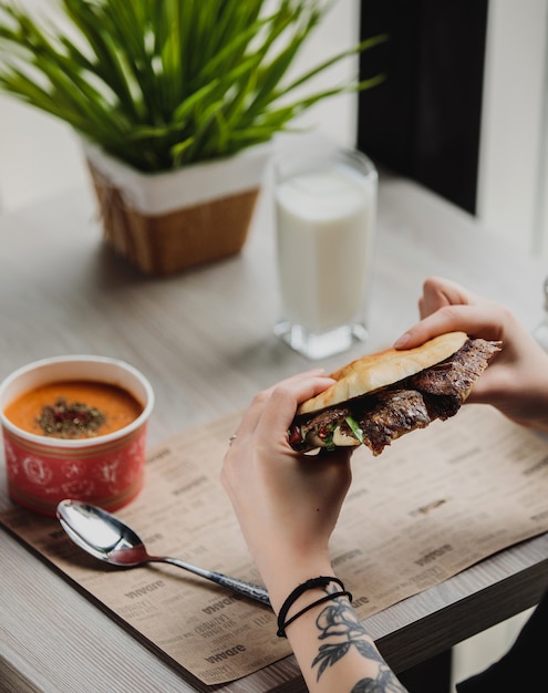 Free photo side view of a person eating doner kebab in pita bread at the table