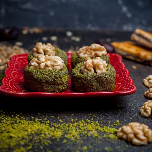 Free photo side view pistachio cookies in red plate on black background.