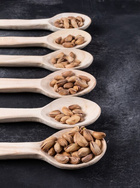 Side view of pistachios on wooden spoons on dark  vertical