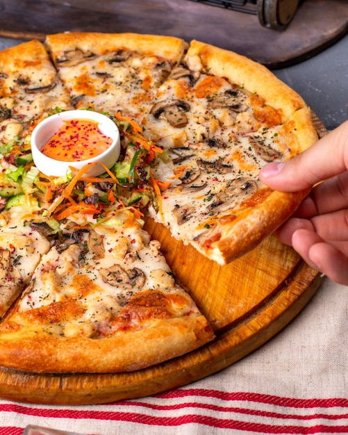 Side view of pizza with chicken and mushrooms served with sauce and vegetables salad on wooden plate