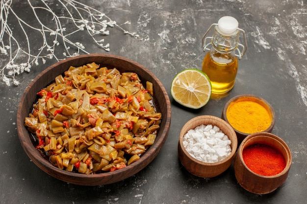 Free photo side view plate of beans and spices bowls of three kinds of colorful spices the plate of green beans next to the tree branches and bottle of oil on the dark table