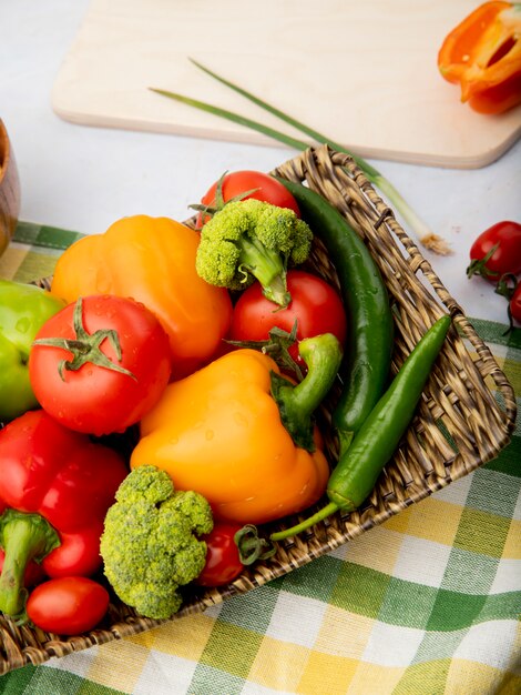 Side view of plate full of vegetables as peppers tomatoes broccoli on plaid cloth on white surface