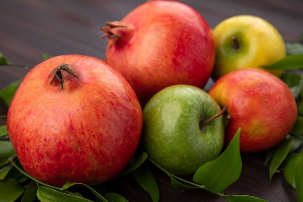 Free Photo side view of pomegranate with colored apples and leaf branches on a wooden surface