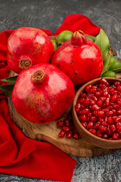 Free photo side view pomegranates seeds of pomegranate three pomegranates with leaves on the wooden board