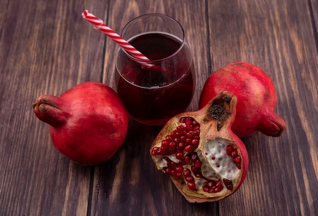 Side view pomegranates with a glass of juice and a red straw on a wooden wall