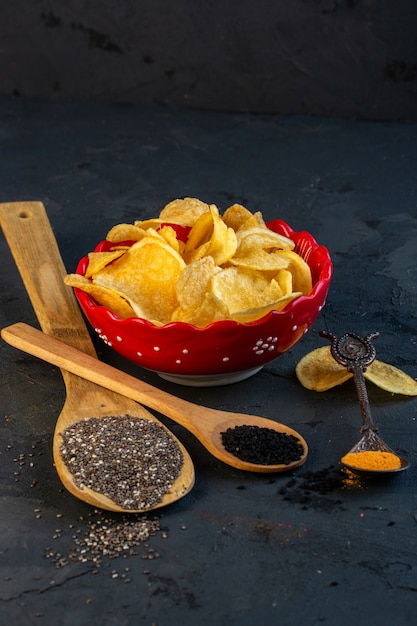 Free photo side view of potato chips in bowl and wooden spoons with black seeds on black