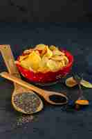 Free photo side view of potato chips in bowl and wooden spoons with black seeds on black