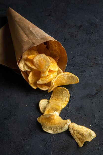 Side view of potato chips scattered from a pepper bag on black