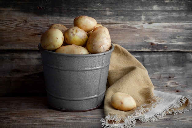 Free photo side view potatoes in gray bucket on dark wooden background. horizontal