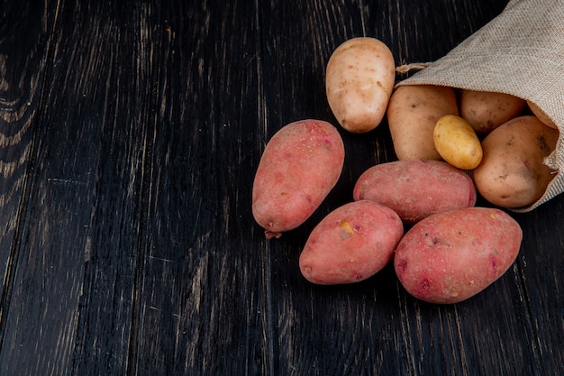 Side view of potatoes spilling out of sack on wooden table with copy space