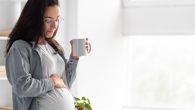 Side view of pregnant woman at home with mug of coffee