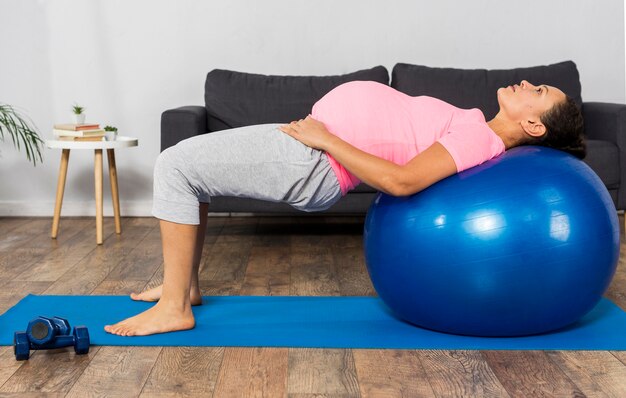 Side view of pregnant woman using ball  to exercise at home