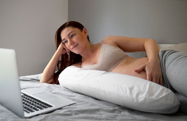 Side view pregnant woman with laptop at home