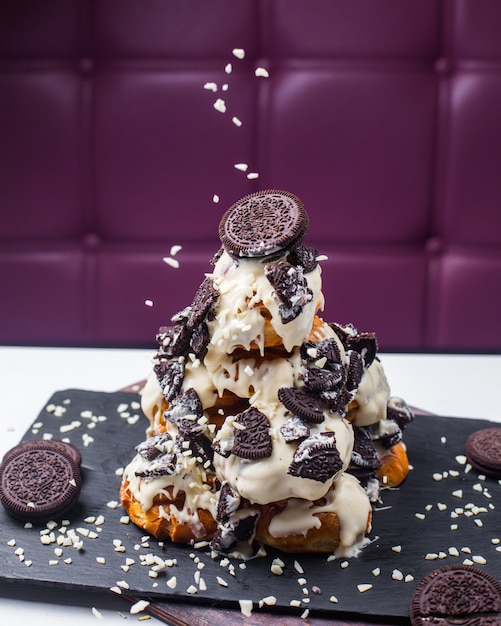 Free Photo side view of profiterole decorated with white chocolate and cookies on a wooden board