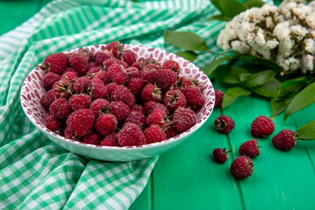 Free Photo side view of raspberries on a plate with flowers on a green checkered towel on a green surface