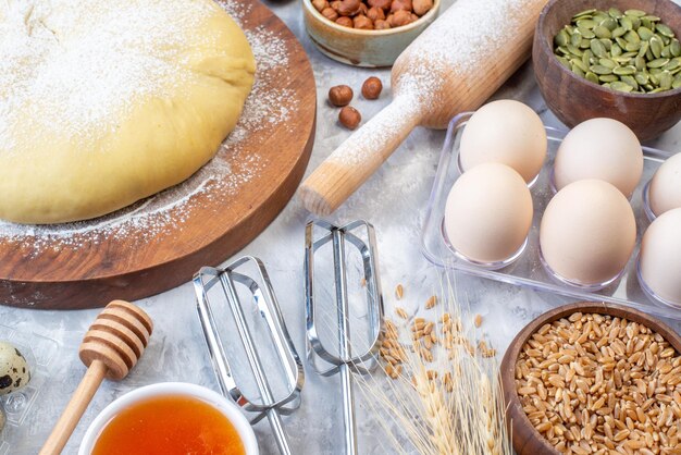 Side view of raw pastry flour on round board grater fresh fruits eggs honey on gray background