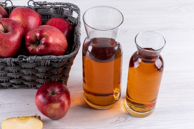 Free photo side view red apples in basket with juice on white wooden table