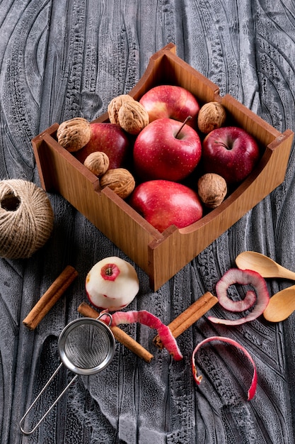 Free photo side view red apples in crate with cinnamon and walnuts on gray wooden