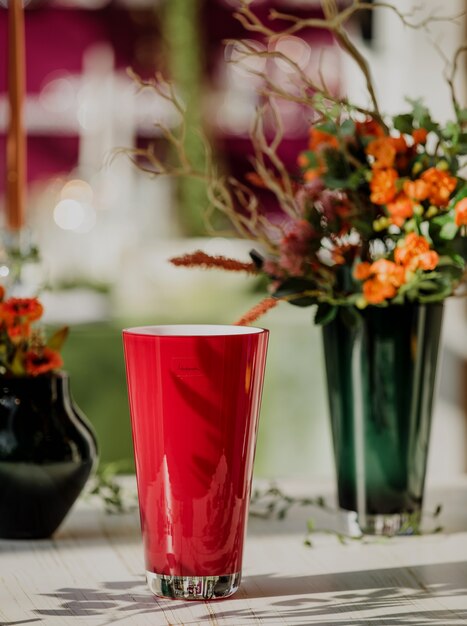 Side view of red color glass for water or juice on the table with flowers in a vase on wall