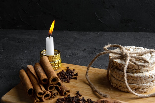 Free photo side view of rice breads tied with rope and cinnamon stick with a burning candle on wooden board on black