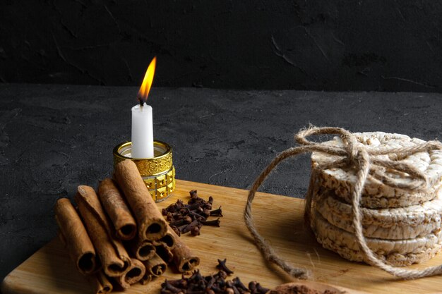 Side view of rice breads tied with rope and cinnamon stick with a burning candle on wooden board on black