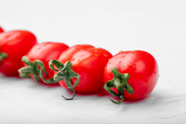 Side view of ripe fresh cherry tomatoes with water drops on white background