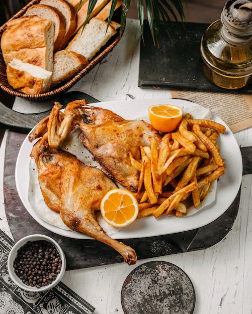 Side view of roasted chicken with french fries in white plate on a wooden cutting board