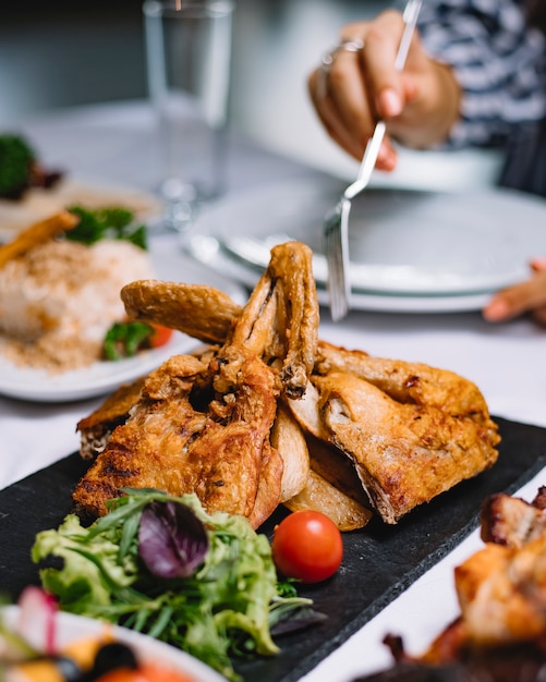 Free photo side view of roasted chicken with herbs and cherry tomato on a black board