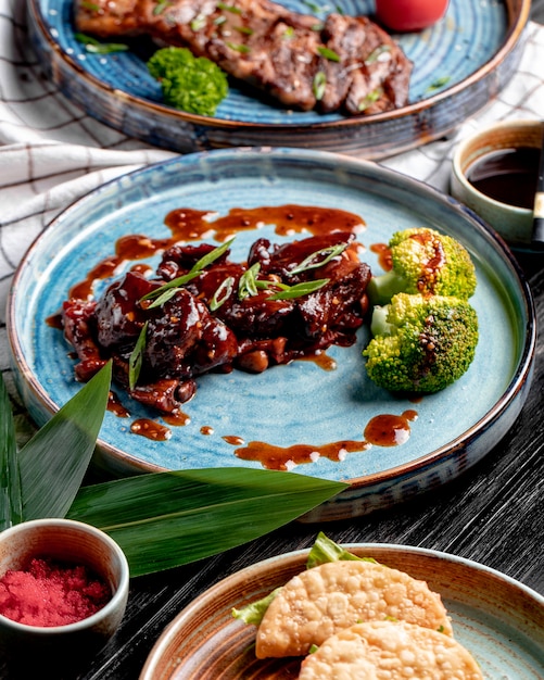 Free photo side view of roasted chicken with sweet and sour sauce and broccoli on a plate on plaid tablecloth