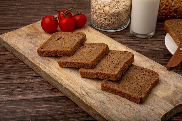 Free photo side view of rye bread slices and tomatoes on cutting board on wooden background