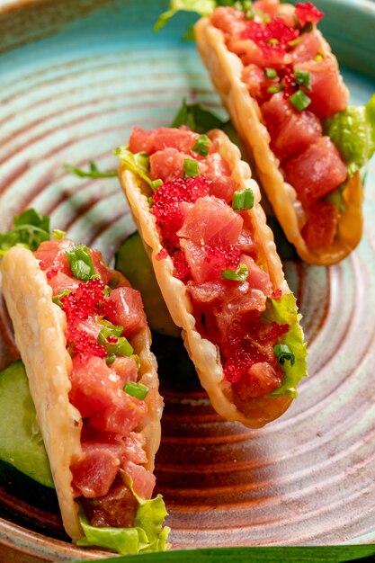 Side view of salmon tacos with red caviar and green onion on a plate