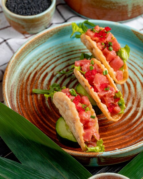 side view of salmon tacos with red caviar and green onion on a plate