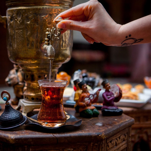 Side view samovar with glass of tea and figurines and human hand in table on restaurant