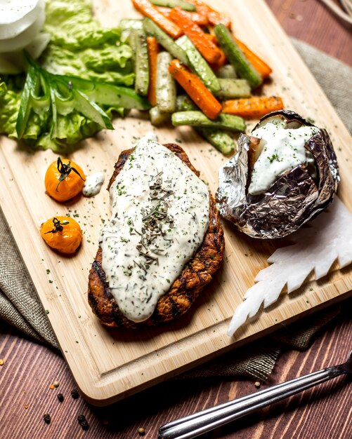 Side view schnitzel with cream cheese with baked potatoes in foil and with vegetables on a board