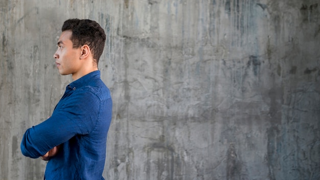 Side view of a serious young man standing against grey concrete background