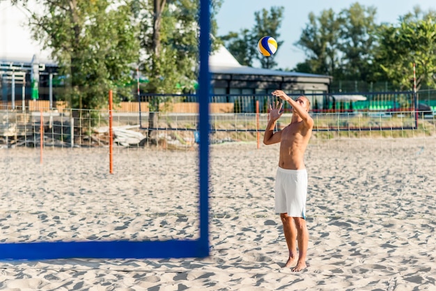 Free Photo side view of shirtless male volleyball player practicing with ball on beach