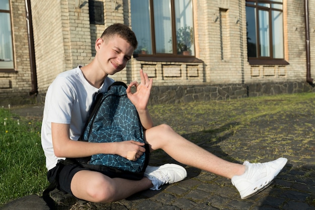 Free photo side view shot sitting teenage boy holding a backpack